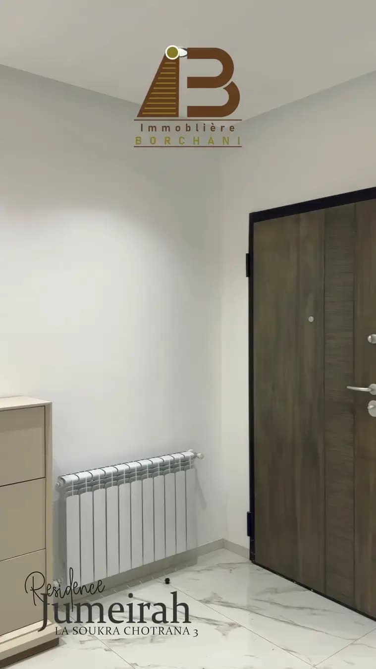 Still from a vertical video filmed inside the Résidence Jumeirah, La Soukra Chotrana 3: wooden front door, radiator and marble floor, with the Borchani logo