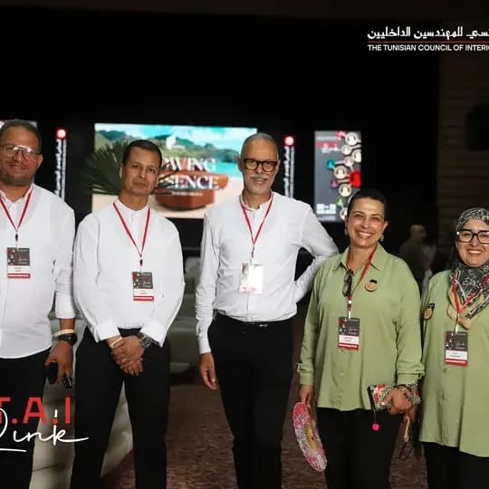 Five participants wearing badges in front of the stage at a CTAI event, with a large LED screen and a vertical screen behind them